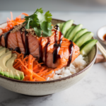 A salmon rice bowl with fresh avocado slices, julienned carrots, cucumber, sesame seeds, and soy sauce on the side.